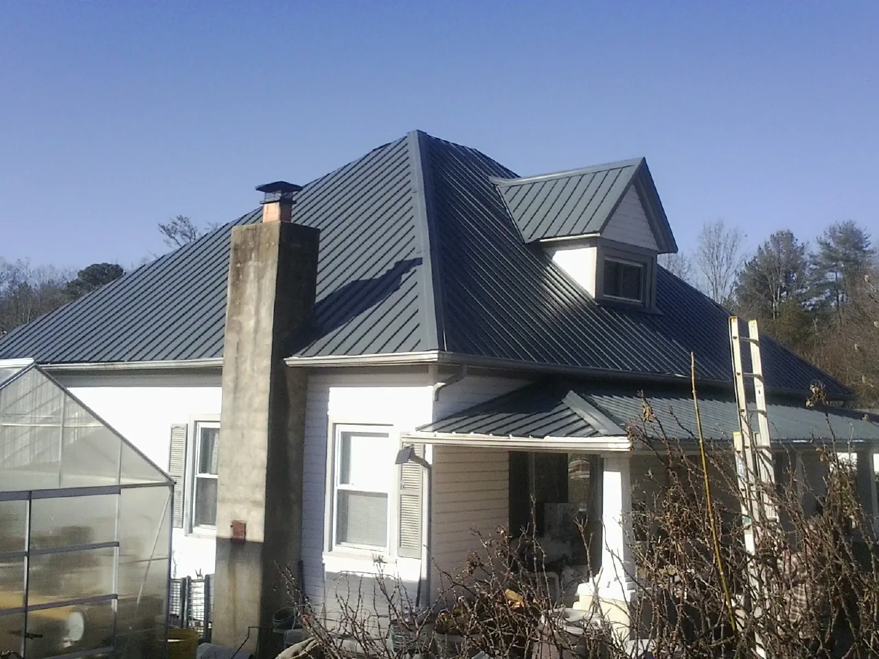 Dark blue standing seam metal roof on a white farmhouse with dormer — Slate & Tile Roof Repair by Roofing Brothers in Loranger