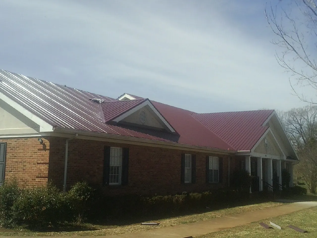 Red metal roof with gabled entries on a long brick building, from a Hail Damage Roof Repair job in Loranger