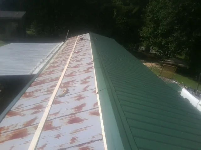 Old rusted panels beside newly installed green metal roofing — Wind Damage Roof Repair by Roofing Brothers in Loranger