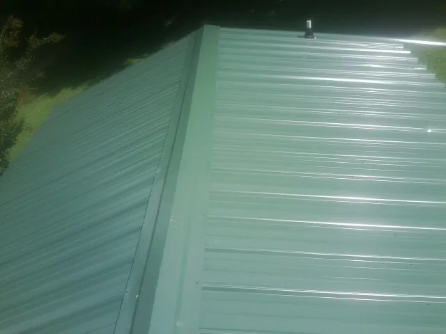 New green metal panels meeting at the ridge of a roof — Flat Roof Repair work by our crew in Loranger