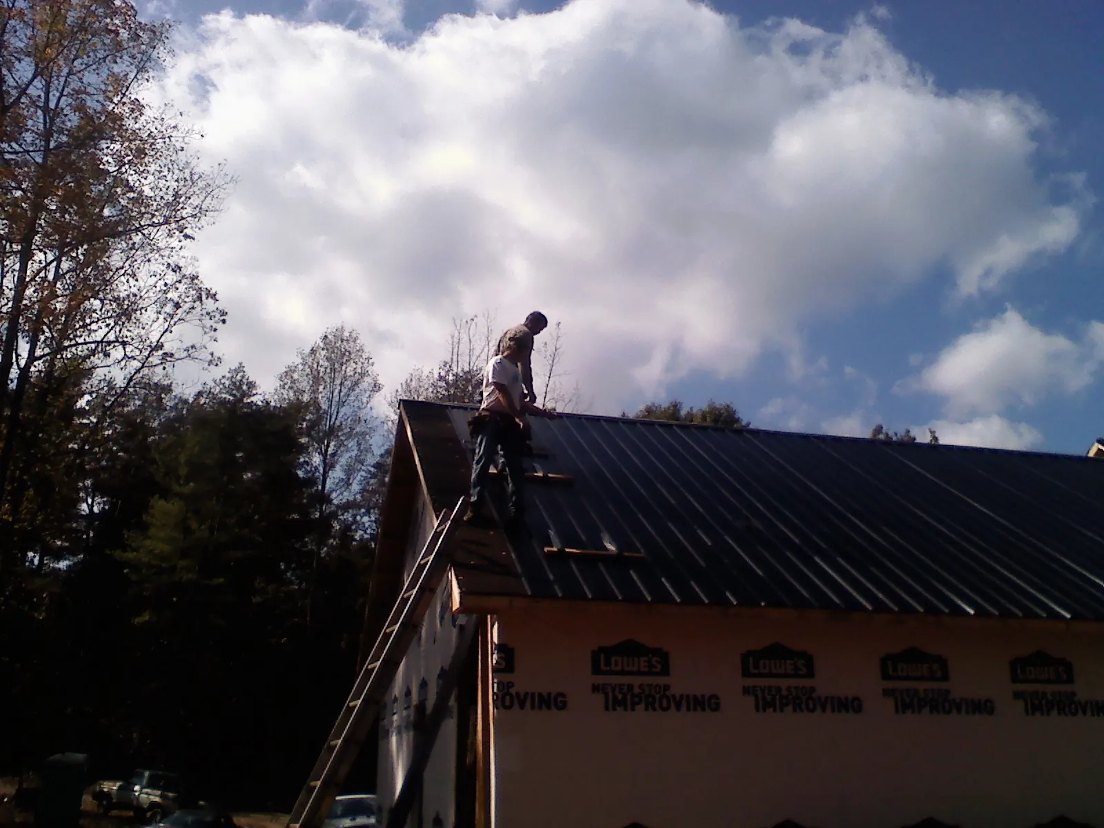 Roofer fastening dark metal panels high against a cloudy sky, from a Roof Inspection job in Loranger