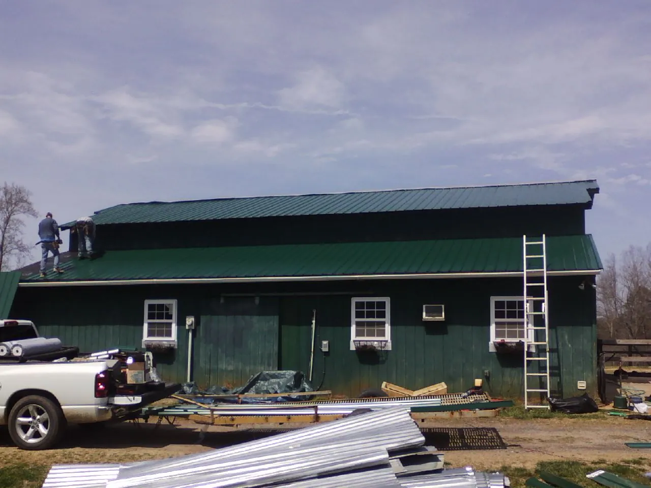 Crew installing green metal roofing on a large green barn in Loranger