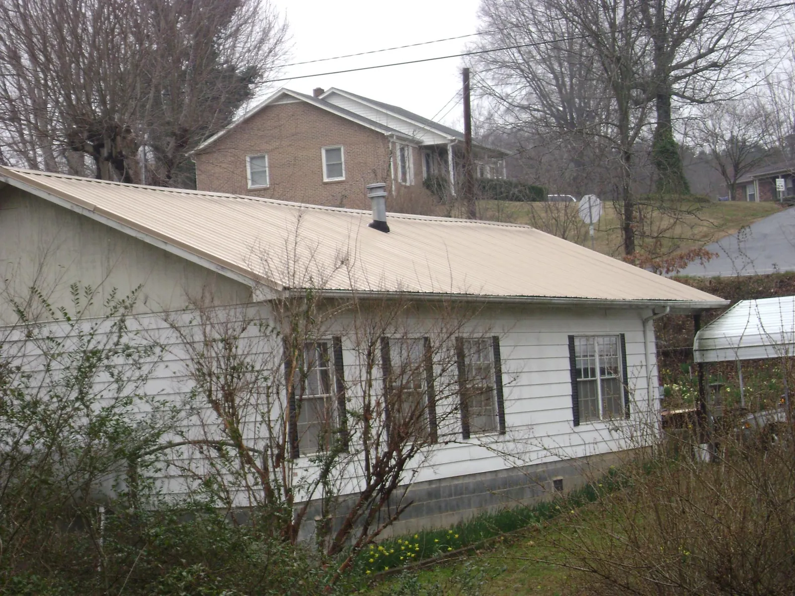 Tan metal roof on a white sided house set into a hillside — Commercial Roofing by Roofing Brothers in Loranger